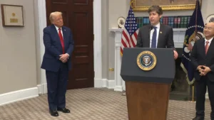 Donald Trump stands to the side as OpenAI CEO Sam Altman delivers a speech from a lectern at the White House.